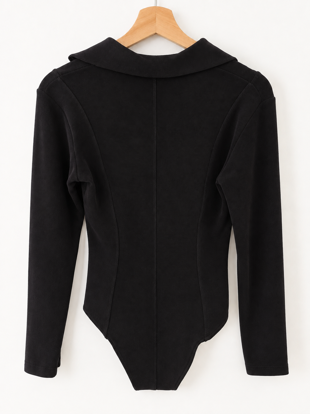 A black long-sleeve bodysuit with a mock neck and side seam details, hanging on a wooden hanger against a plain white background.